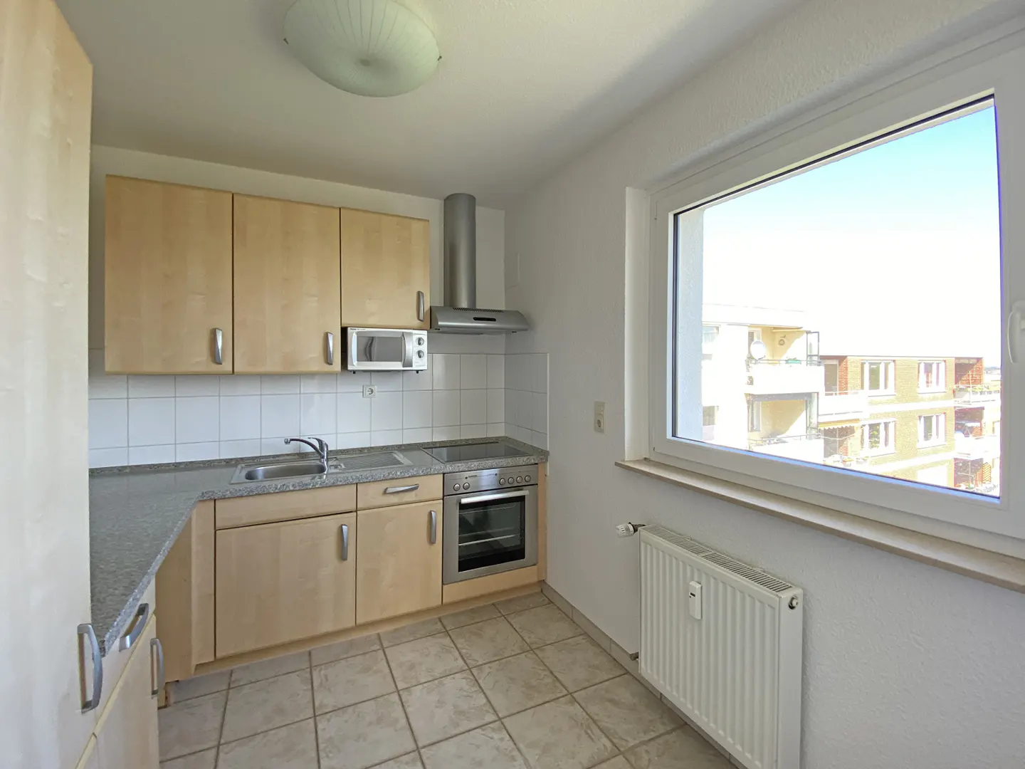Bright kitchen with light wood cabinets, stainless steel appliances, and a window view of a building.