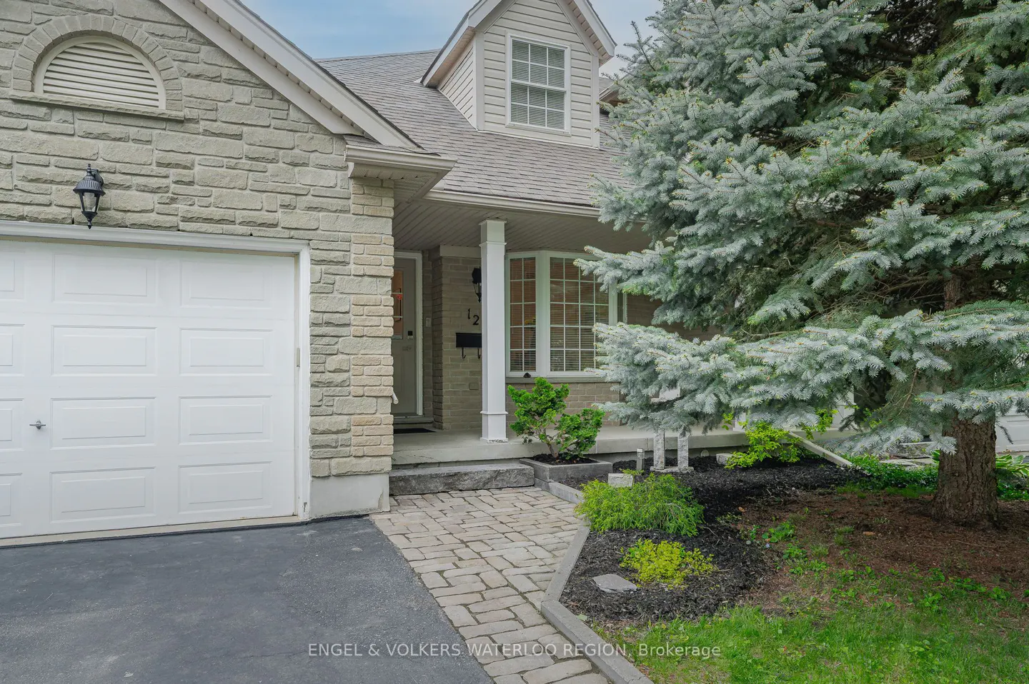 Exterior of a two-story house with a white garage door, stone facade, and a large blue spruce tree.