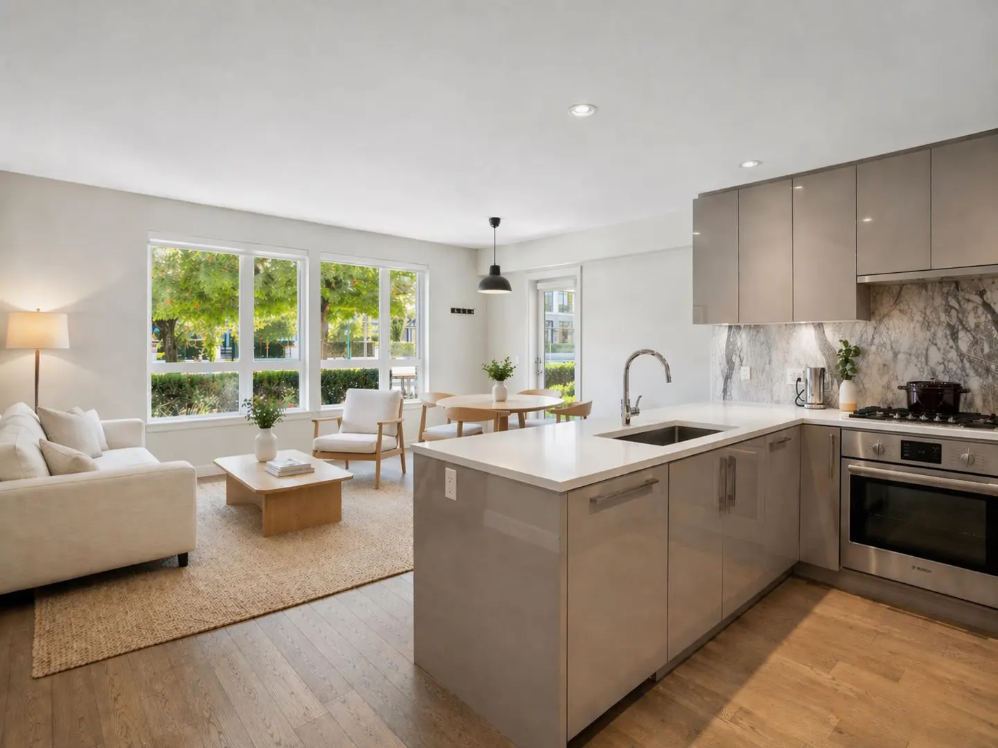 Open-concept living space with a kitchen island, dining table, and living room with large windows.