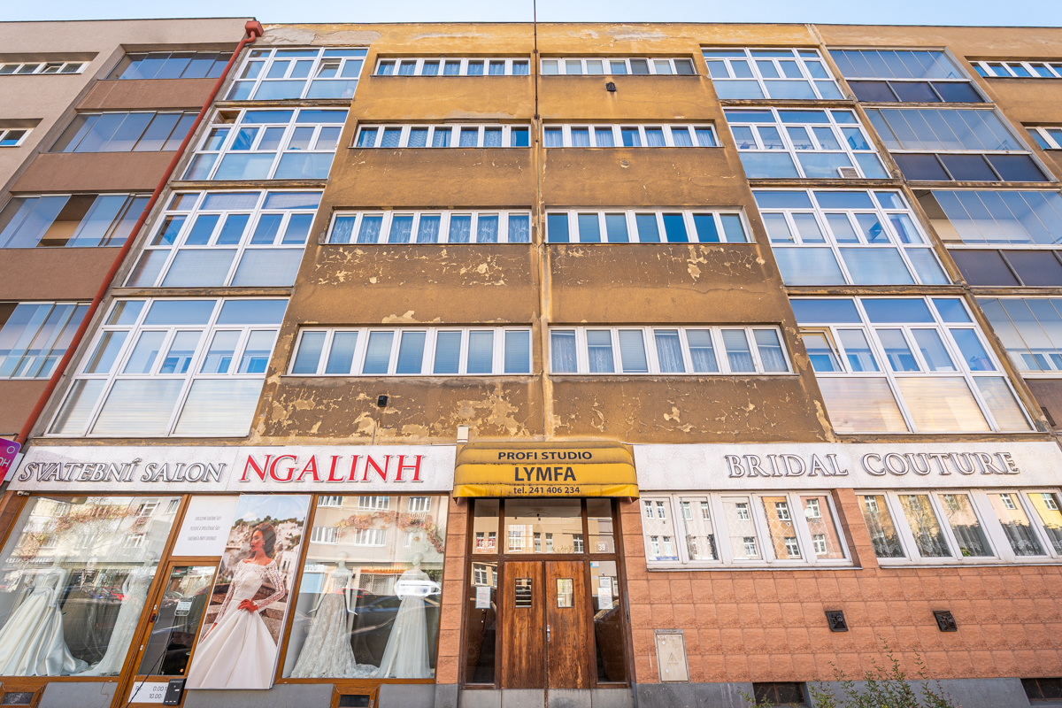 Exterior of a multi-story building with bridal shops on the ground floor. The building is tan with white-framed windows.