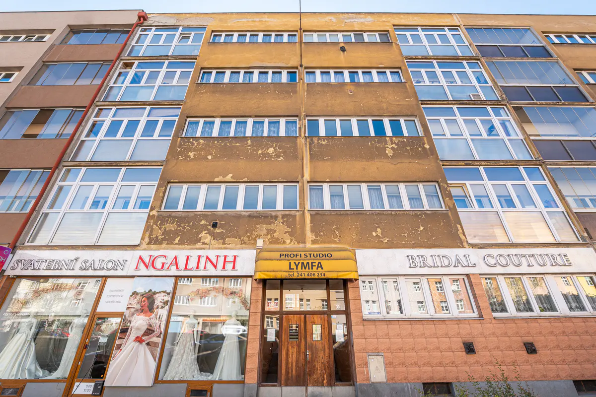 Exterior of a multi-story building with bridal shops on the ground floor. The building is tan with white-framed windows.