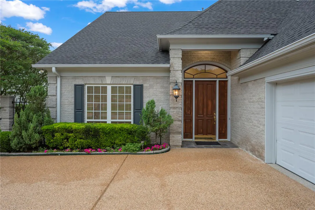 Front exterior of a light brick house with a dark wood door, gray shutters, and a gray roof.