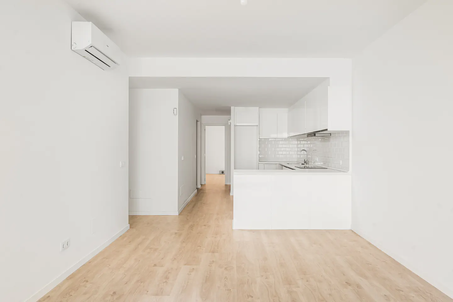 Minimalist white kitchen with light wood floors, an air conditioning unit, and an open-plan layout.