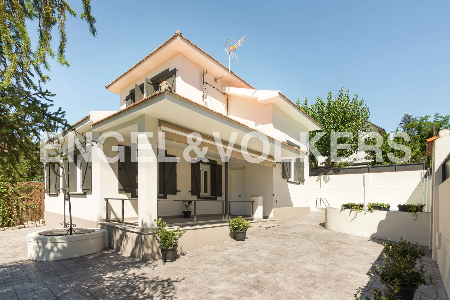 Exterior of a two-story house with a light pink facade, dark shutters, and a well in the front yard.