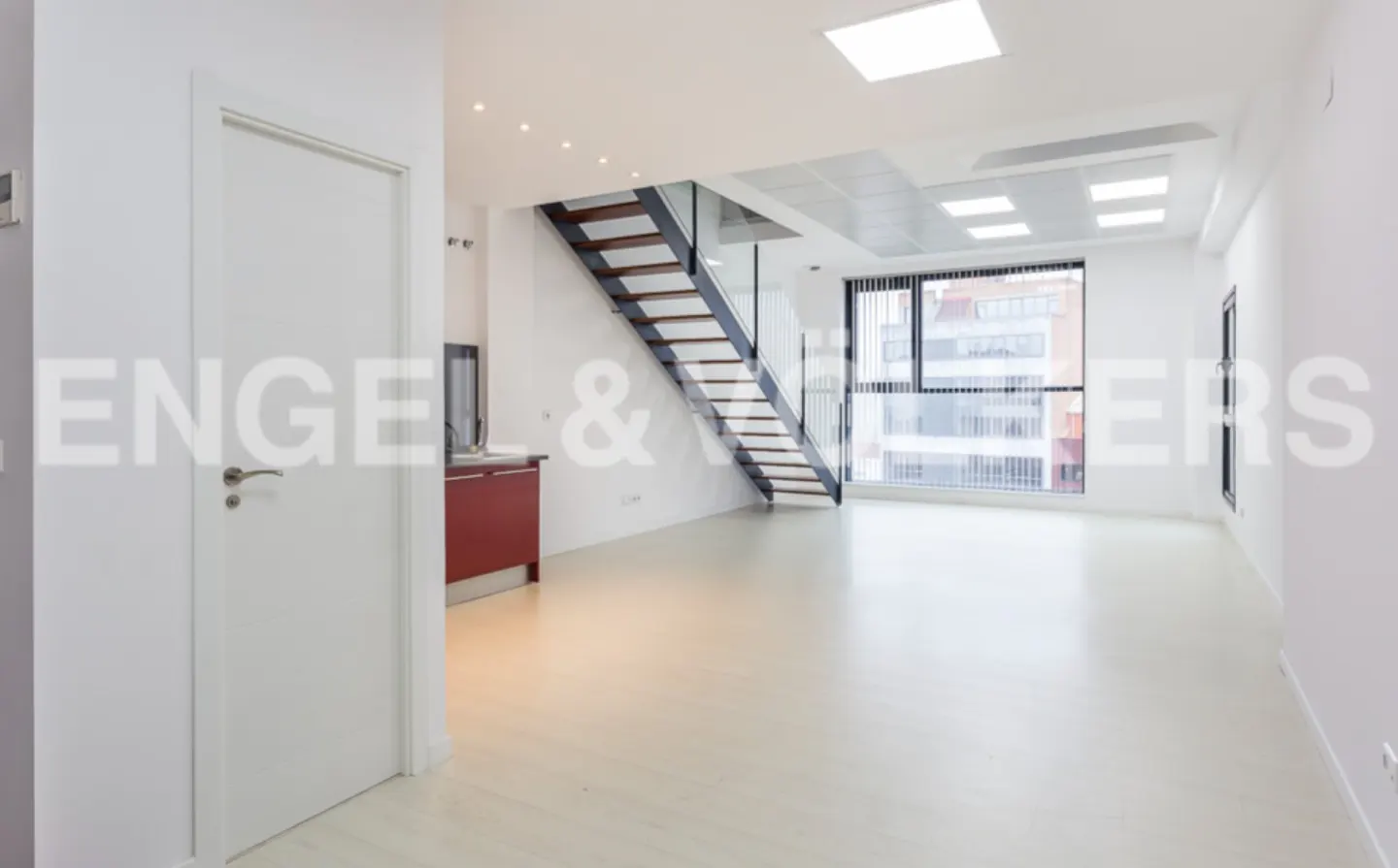 Bright, modern apartment interior with white walls, light wood floors, and a staircase with glass railings. A red cabinet is visible in the background.