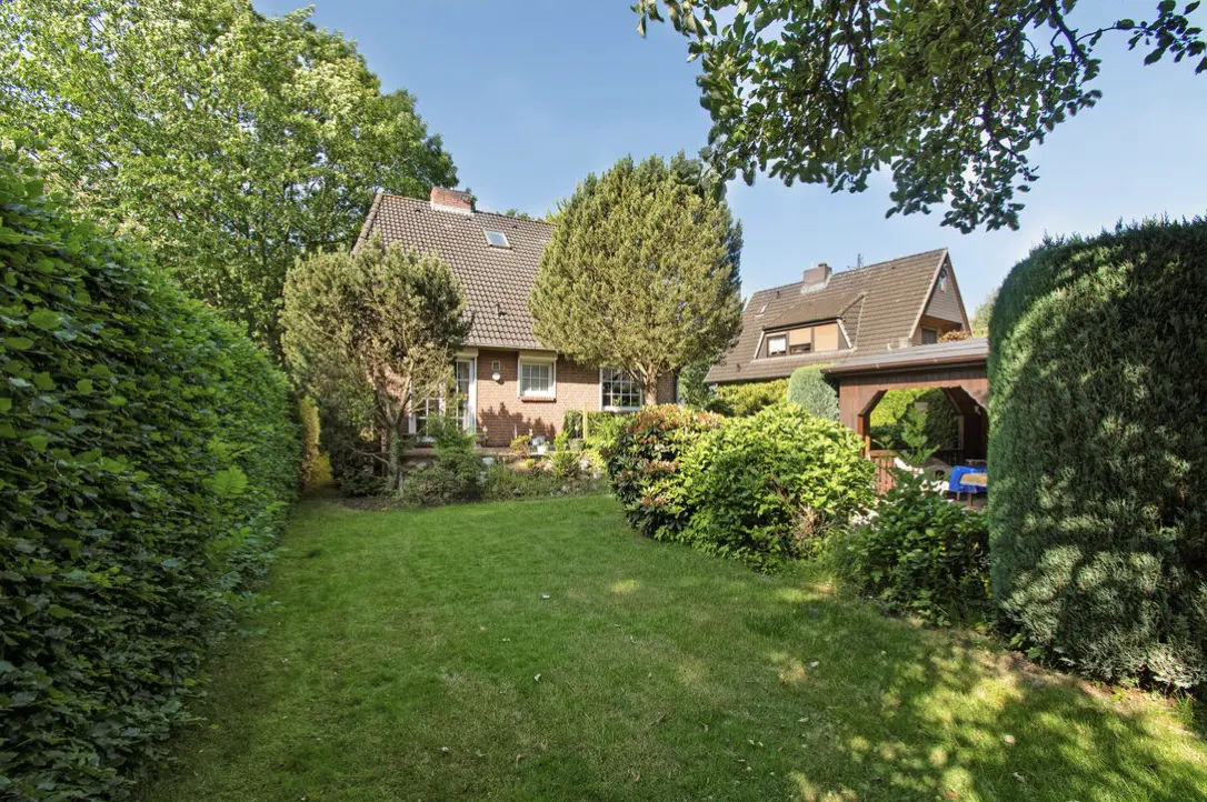 A house with a brown roof and brick walls, surrounded by a green lawn, trees, and bushes.