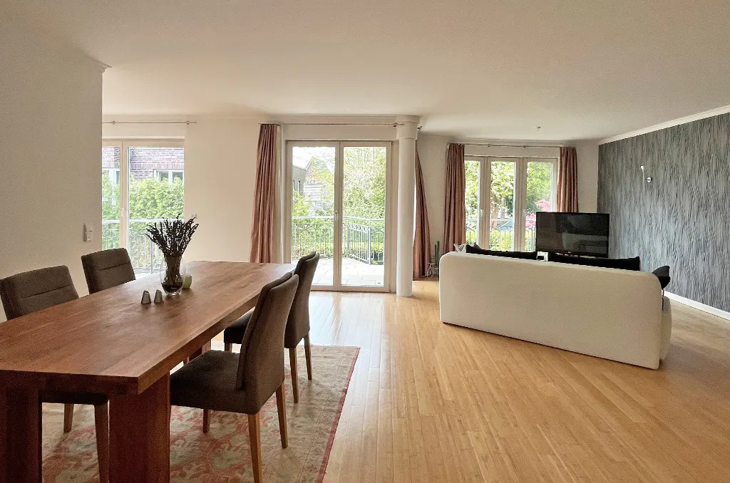 Open-concept living and dining area with wood floors, table with chairs, white sofa, TV, and balcony access.