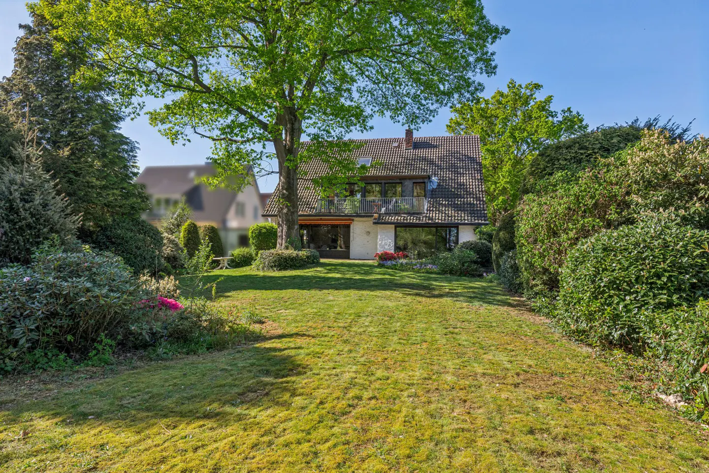 A two-story house with a gray roof and white walls, surrounded by green trees and a large lawn.