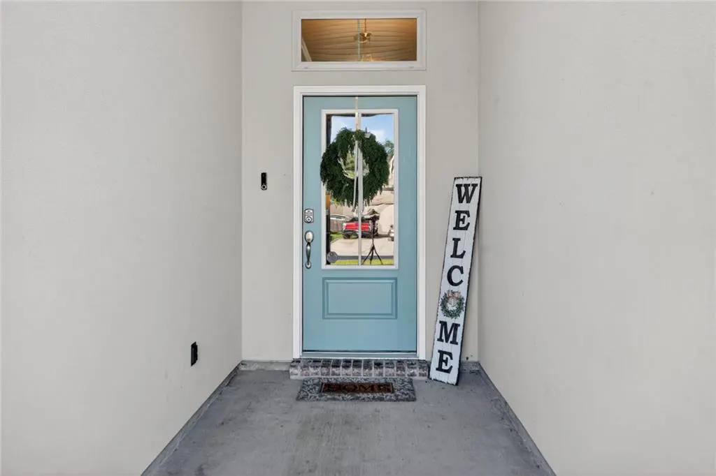 Front door view: Light blue door with glass, wreath, welcome sign, and gray walls.