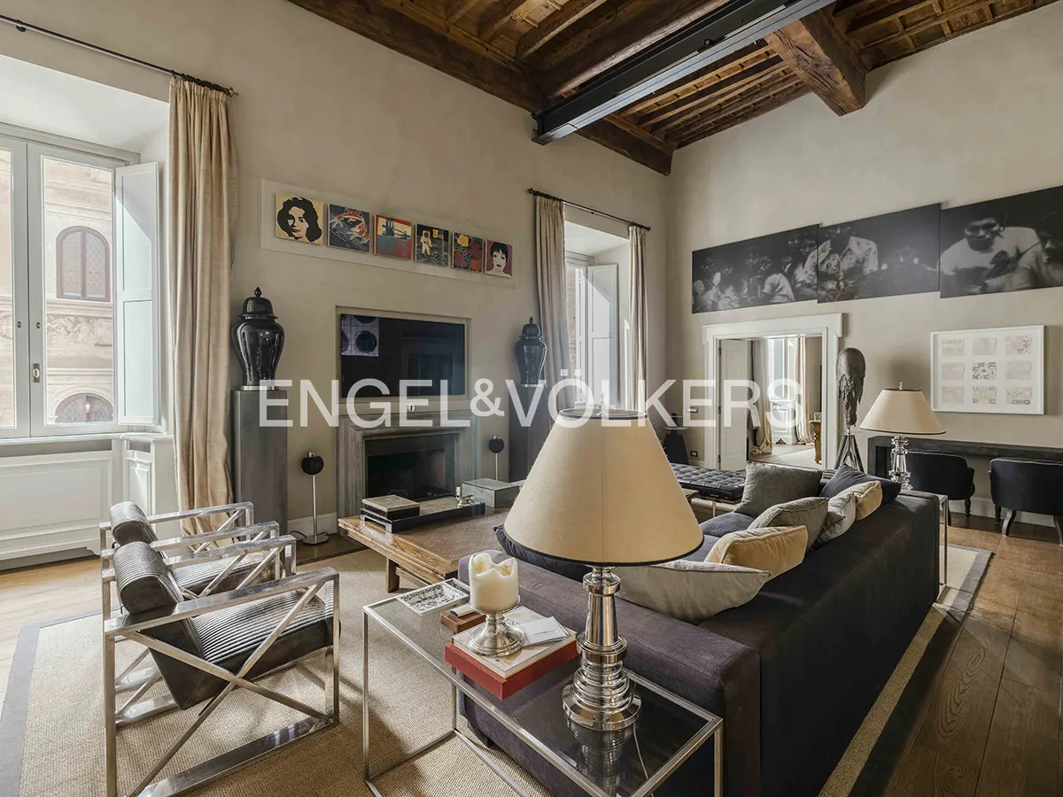 Living room with a gray sofa, metal chairs, and a fireplace. Art hangs above the TV and a doorway leads to another room.