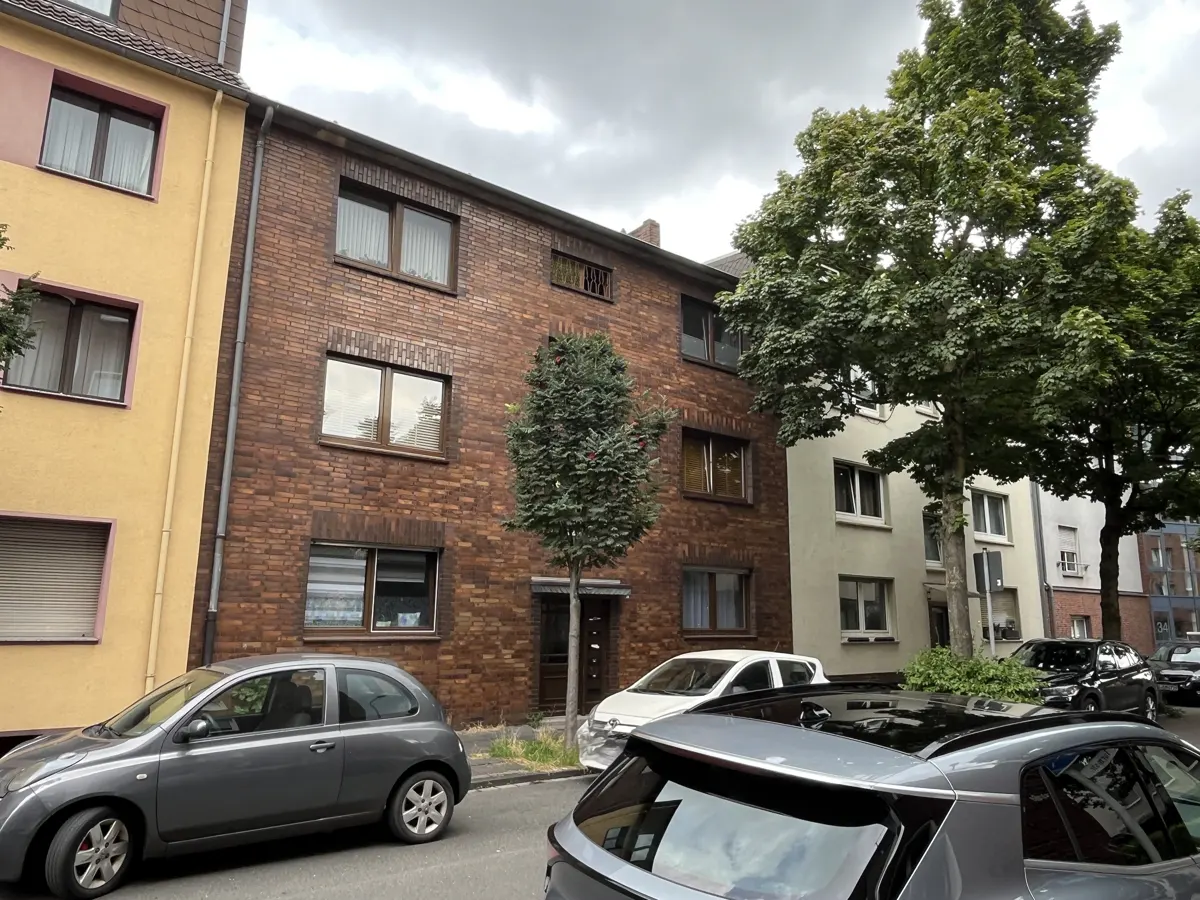 A three-story brick apartment building with parked cars in front.