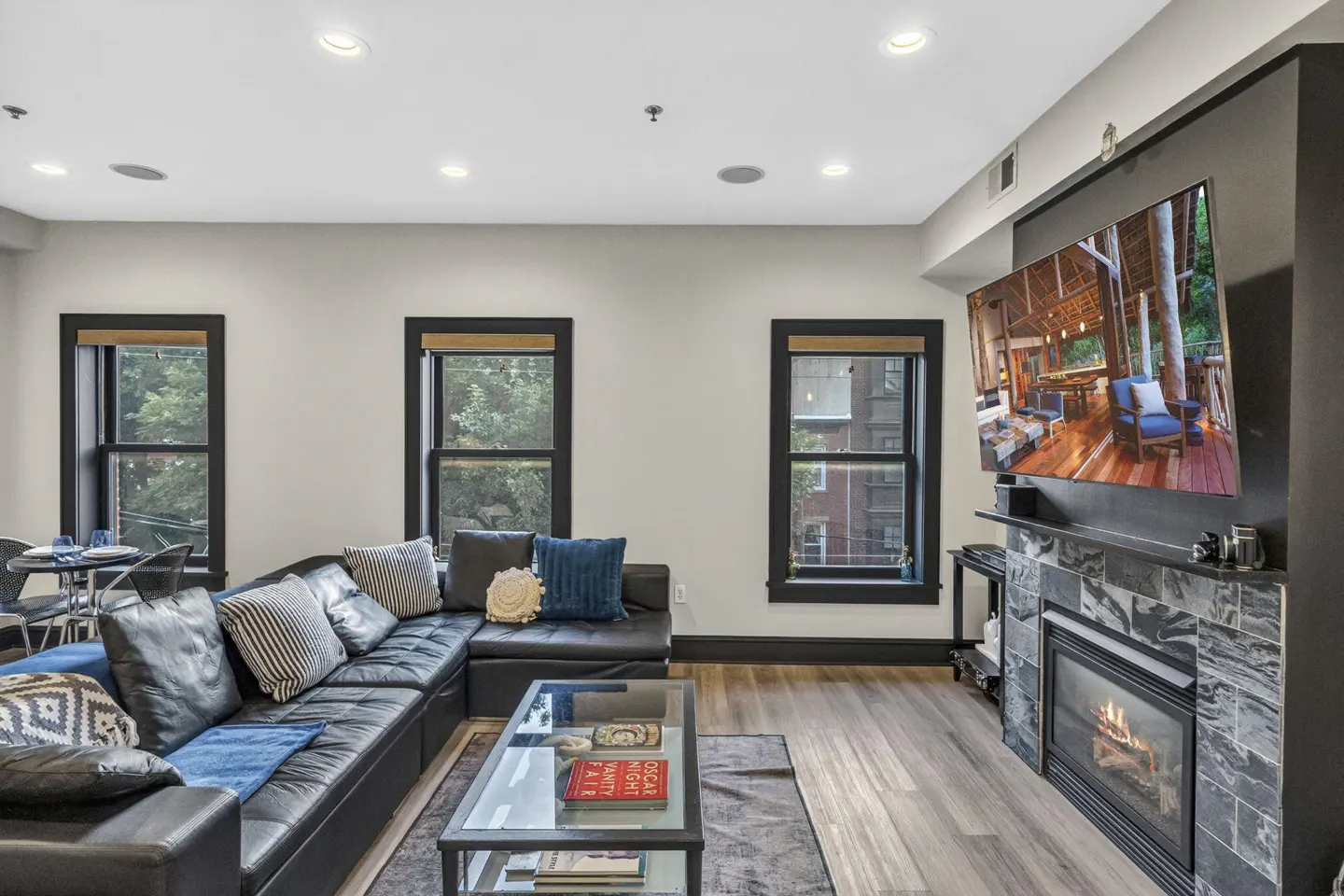 Modern living room with a black leather sectional, glass coffee table, and a fireplace with a mounted television above.