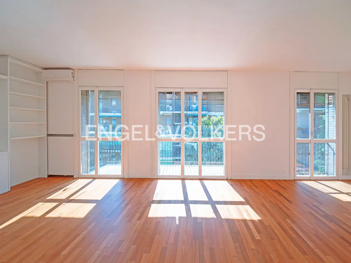 Bright, empty room with light wood floors, white walls, built-in shelving, and large glass doors leading to a balcony.