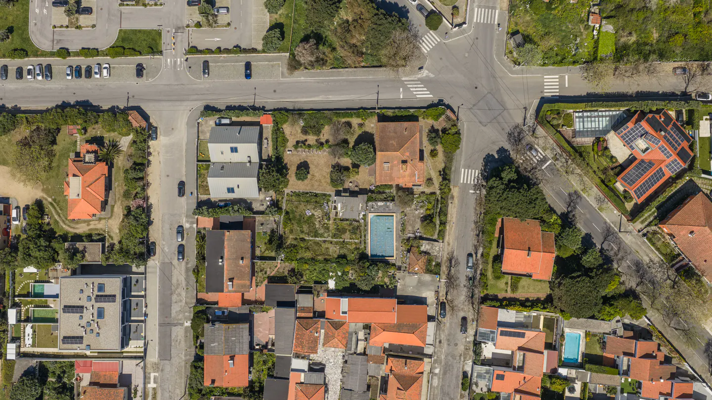 Aerial view of a residential area with houses, roads, and a parking lot. Some houses have pools and solar panels.