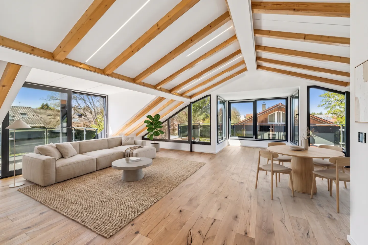 Bright, airy living space with exposed beams, large windows, and light wood floors. A beige sectional sofa sits on a jute rug.