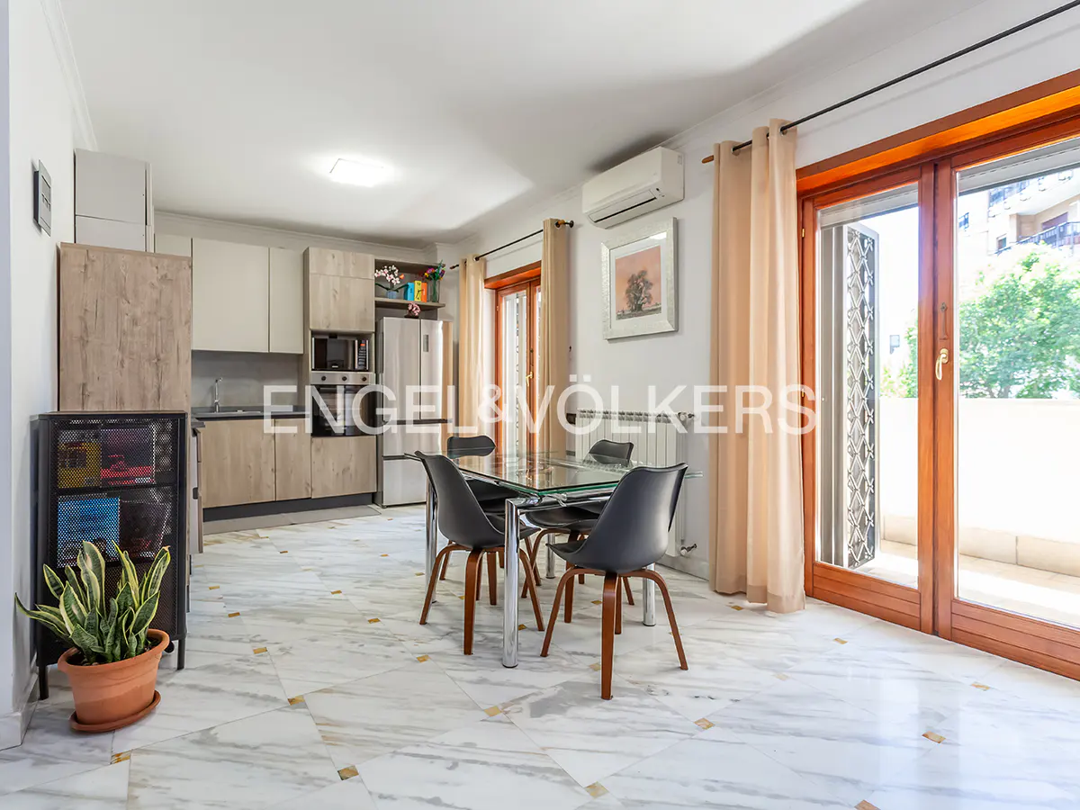 Modern kitchen and dining area with marble floors, glass table, black chairs, and a balcony door with beige curtains.