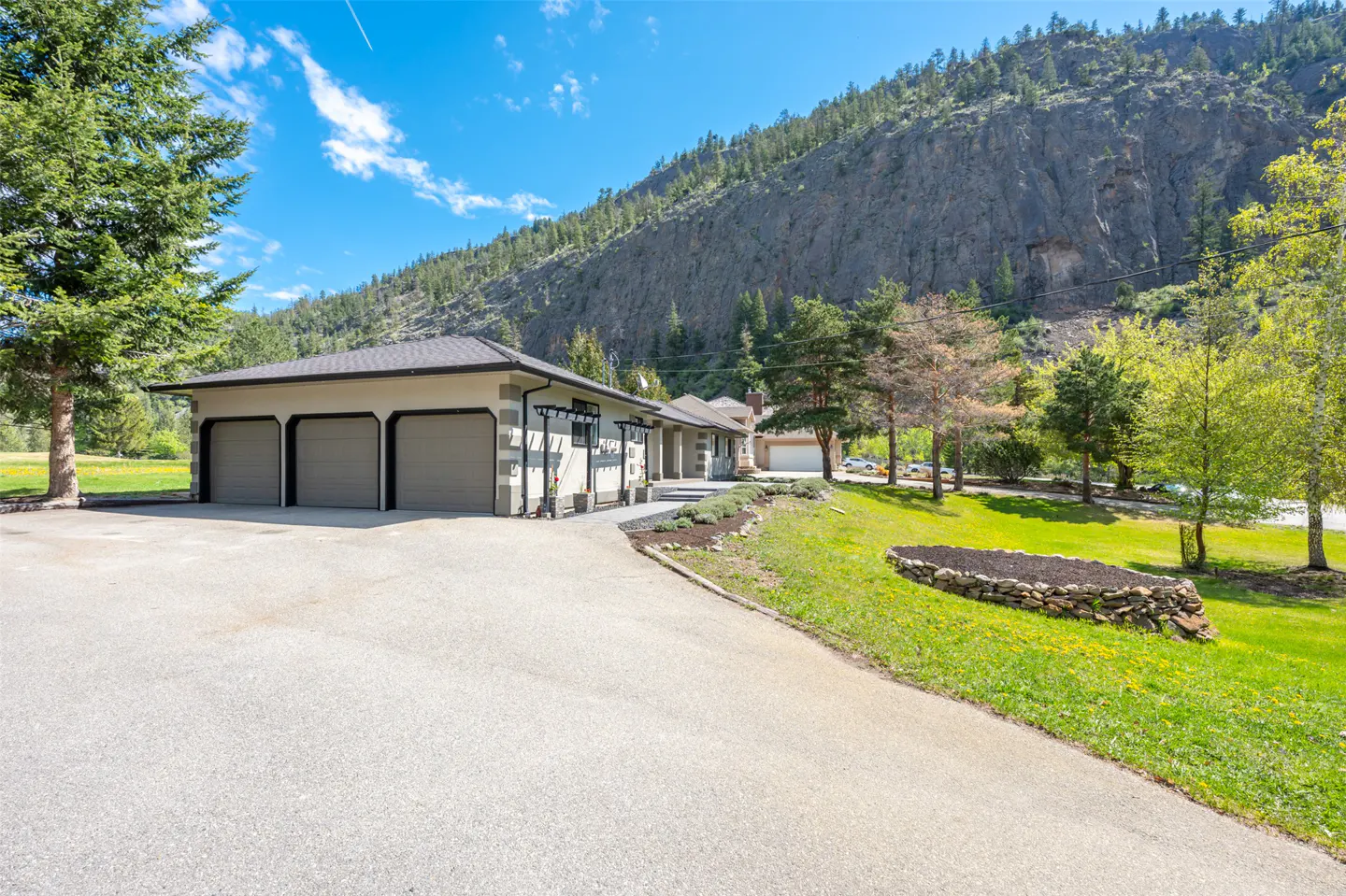 Exterior view of a modern home with a three-car garage, a long driveway, and a mountain backdrop on a sunny day.