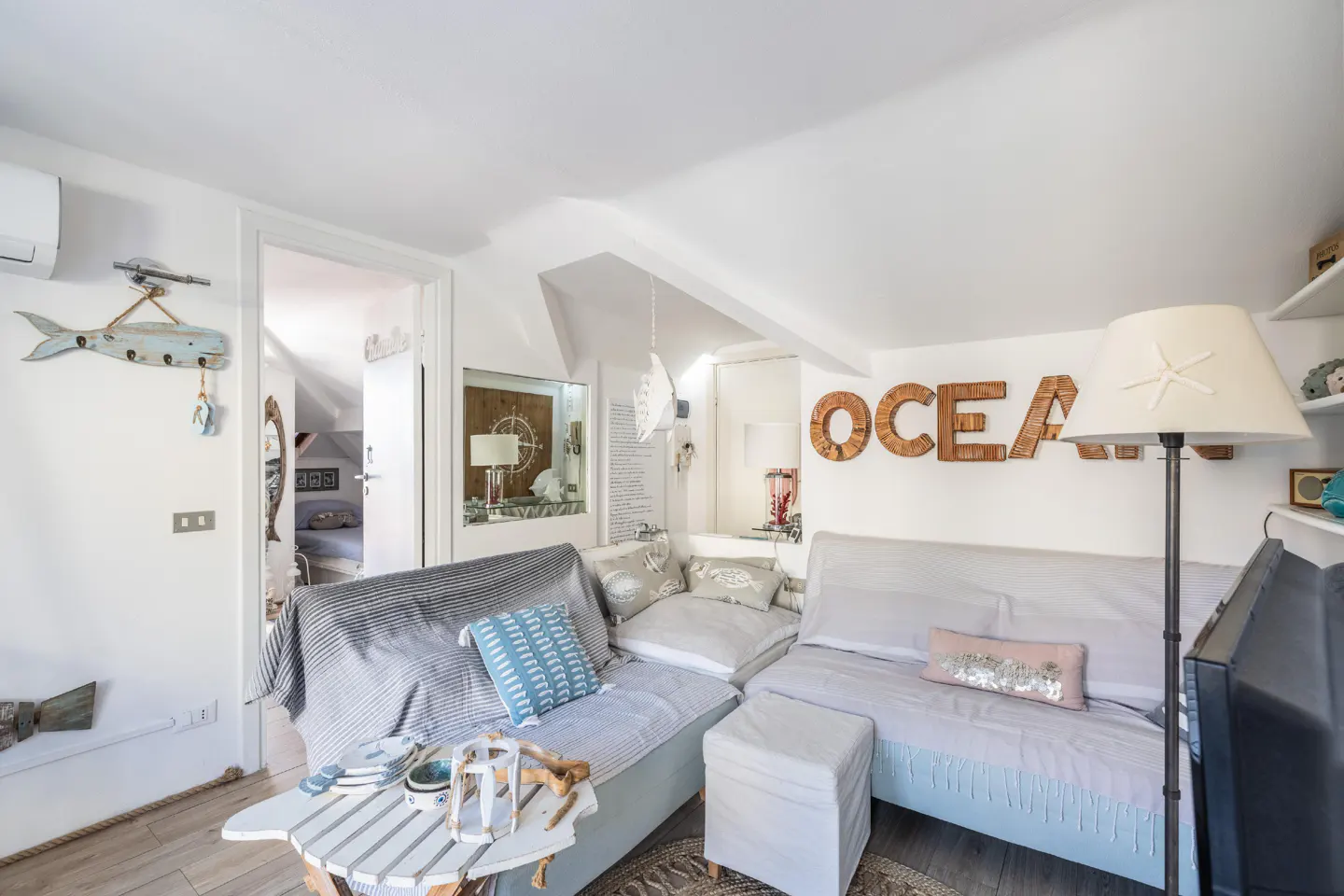 Attic living room with nautical decor. White walls, light blue sofas, and wooden "OCEAN" letters on the wall. Coastal theme.