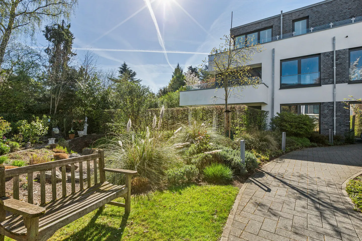 Exterior view of a modern home with a wooden bench in the garden on a sunny day.