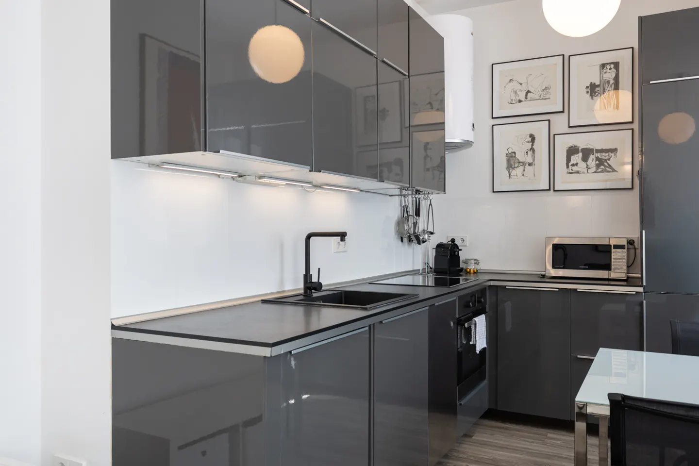 A modern kitchen with gray cabinets, a black sink and faucet, and white walls decorated with framed art.