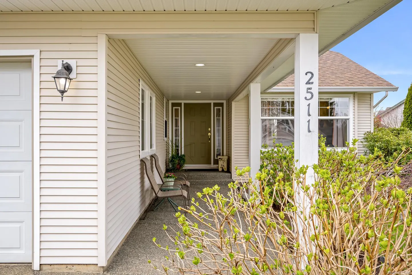 Exterior view of a beige house with a covered porch, chairs, and the house number 2511 on a white pillar.