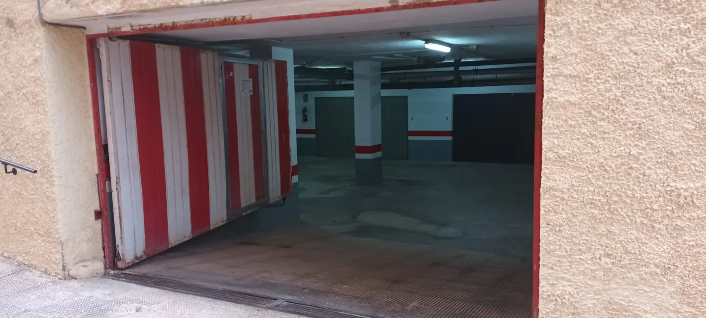 Entrance to an underground parking garage with a red and white striped metal door and concrete walls.