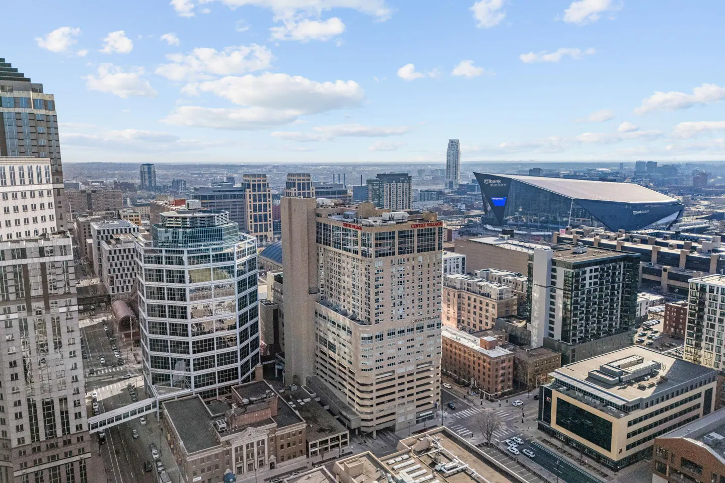 Cityscape view of Minneapolis, Minnesota, featuring modern buildings, roads, and the U.S. Bank Stadium under a blue sky with scattered clouds.