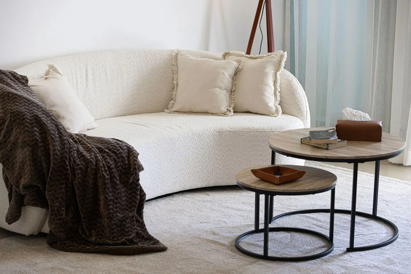 Living room with a white curved sofa, brown throw blanket, and round nesting tables.