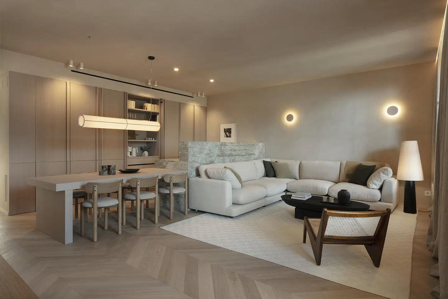 Open-concept living space with a white sectional sofa, dining table with chairs, and herringbone wood floors.