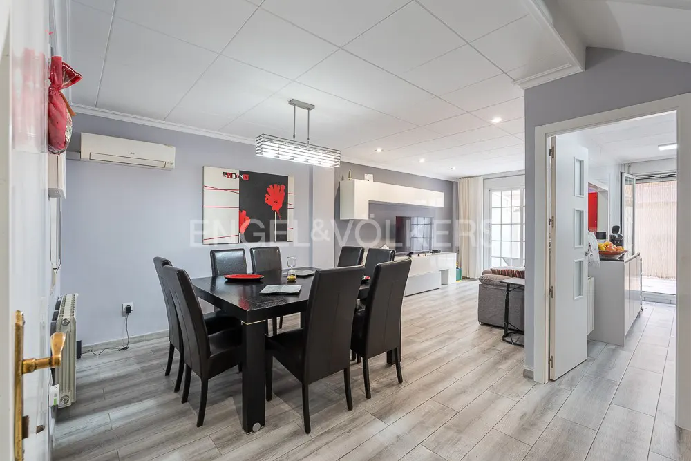 Modern dining area with a black table and six chairs, light wood floors, and abstract art on a light gray wall.