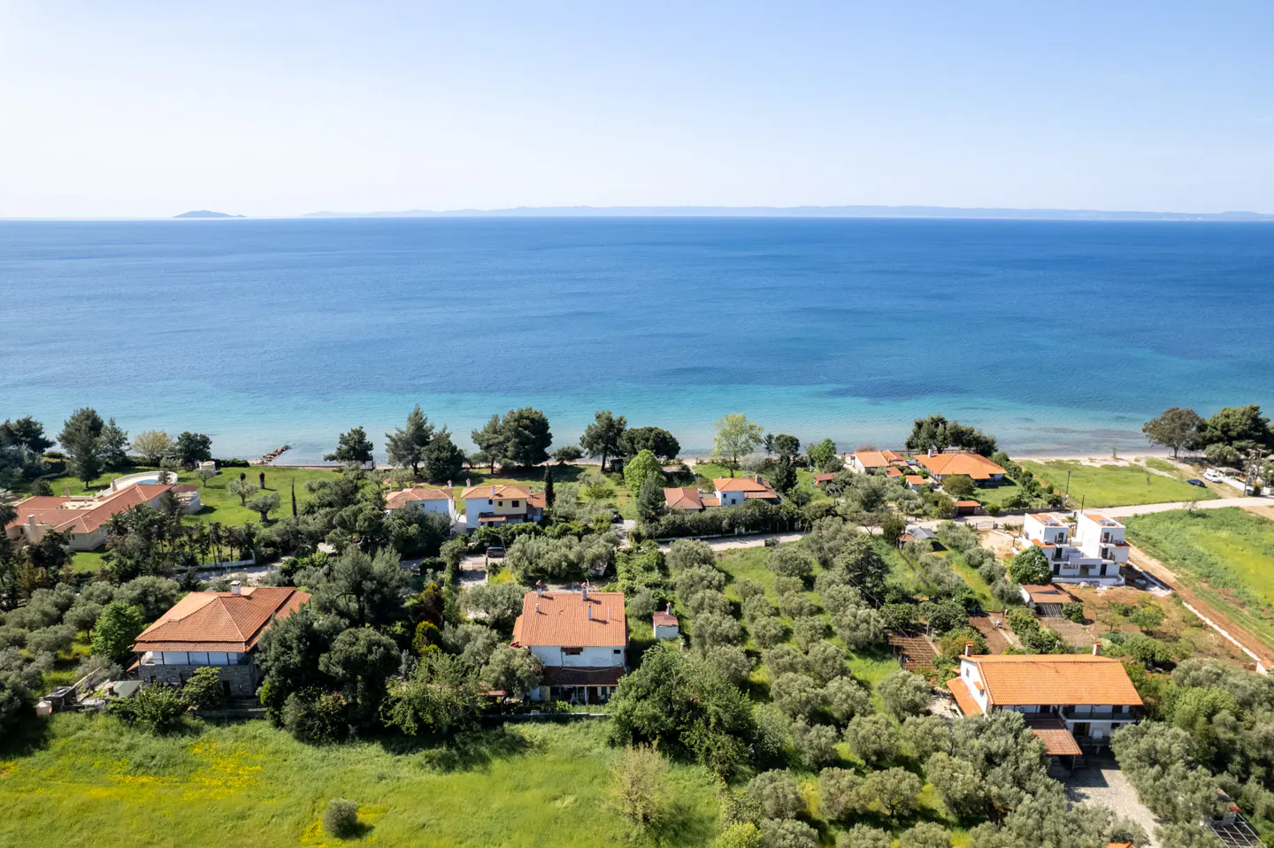 Coastal view of houses with red roofs, green trees, and blue sea under a clear sky.
