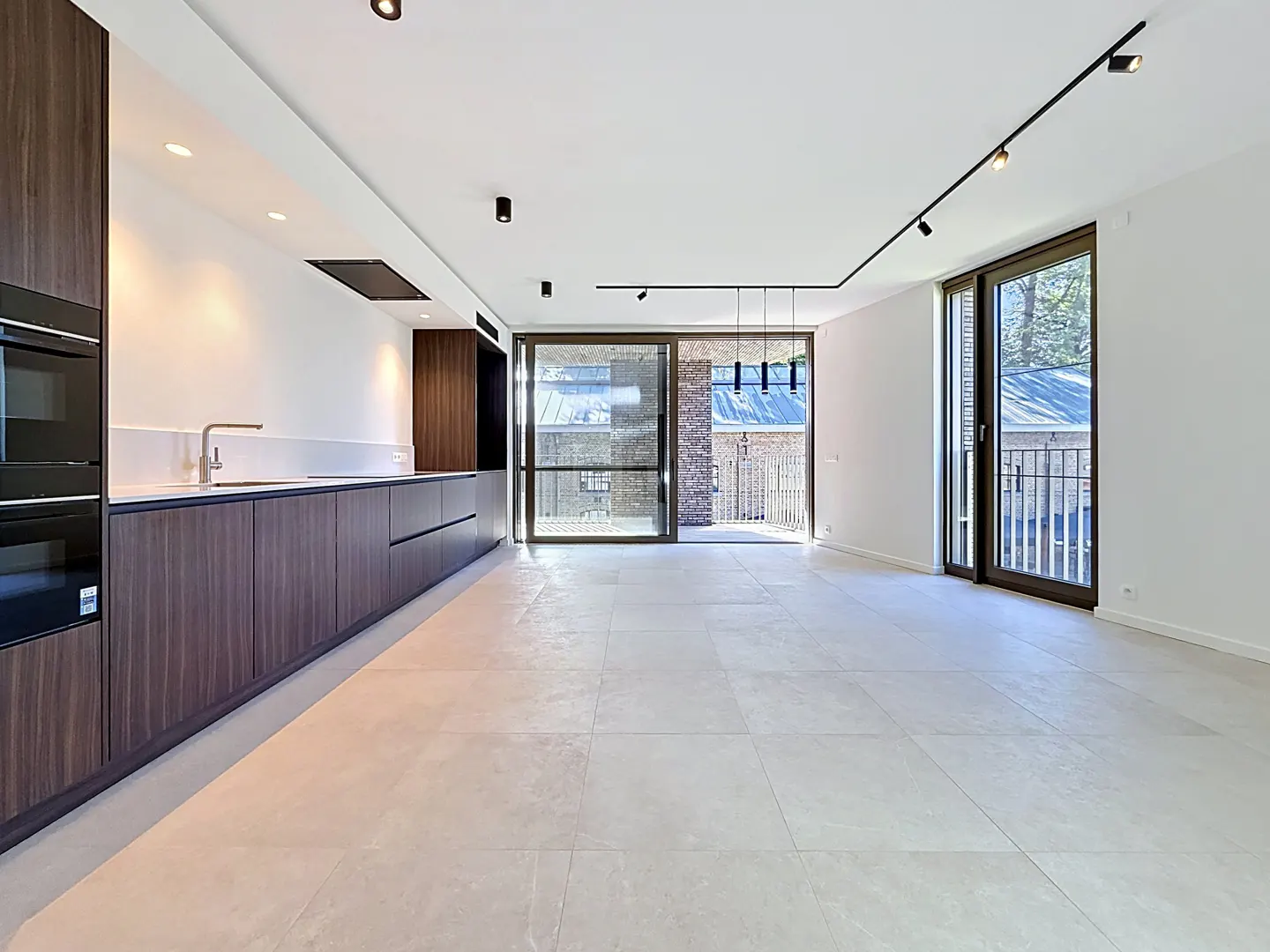 Bright, modern kitchen with dark wood cabinets, white walls, and light tile floors. Sliding glass doors lead to a balcony.