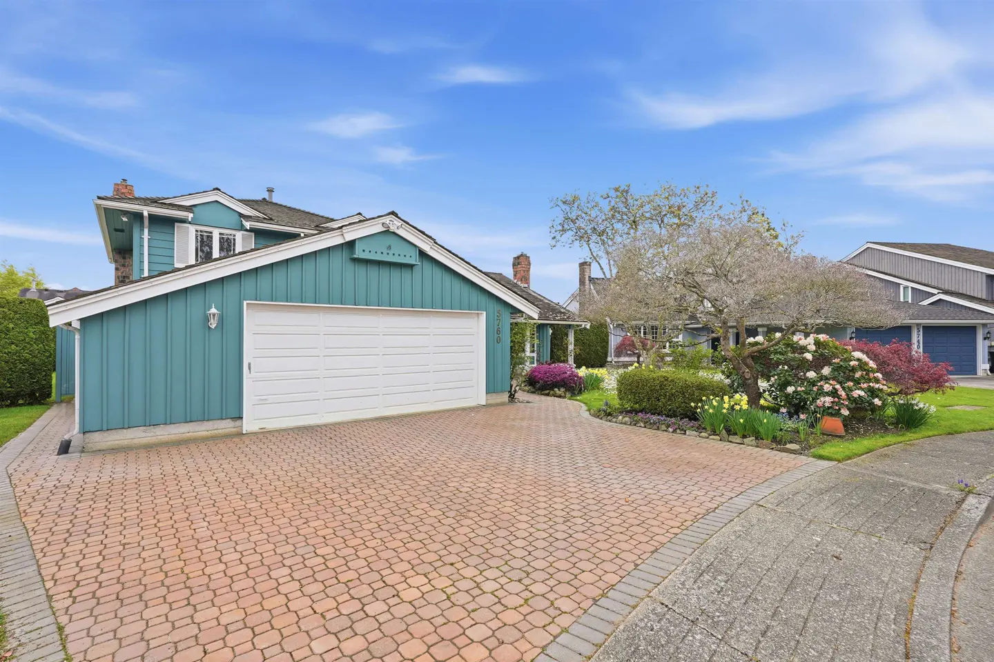 Exterior of a teal house with a white garage door and a brick driveway under a blue sky.