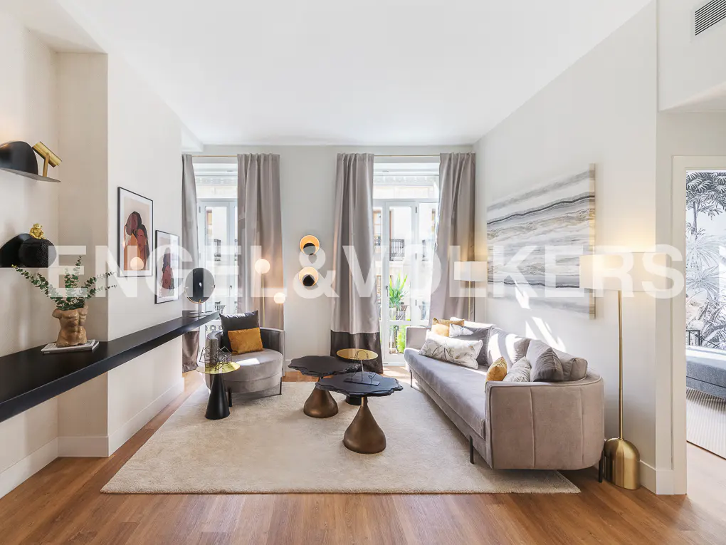 Living room with wood floors, white walls, and gray furniture. A long black shelf holds art. Windows have gray curtains.