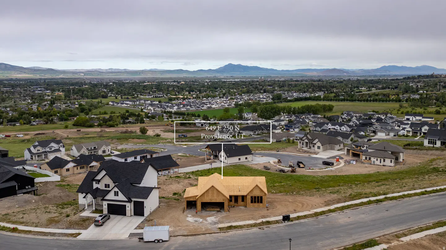 Aerial view of a new housing development with homes in various stages of construction. Mountains are visible in the background.
