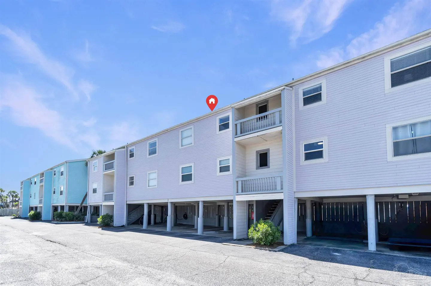 Exterior view of a two-story condo building with balconies, painted in light blue and lavender, under a clear blue sky.