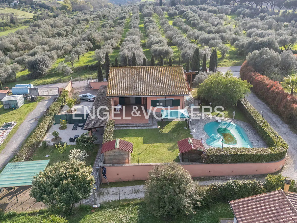 Aerial view of a peach-colored house with a red tile roof, a pool, and an olive grove in the background.