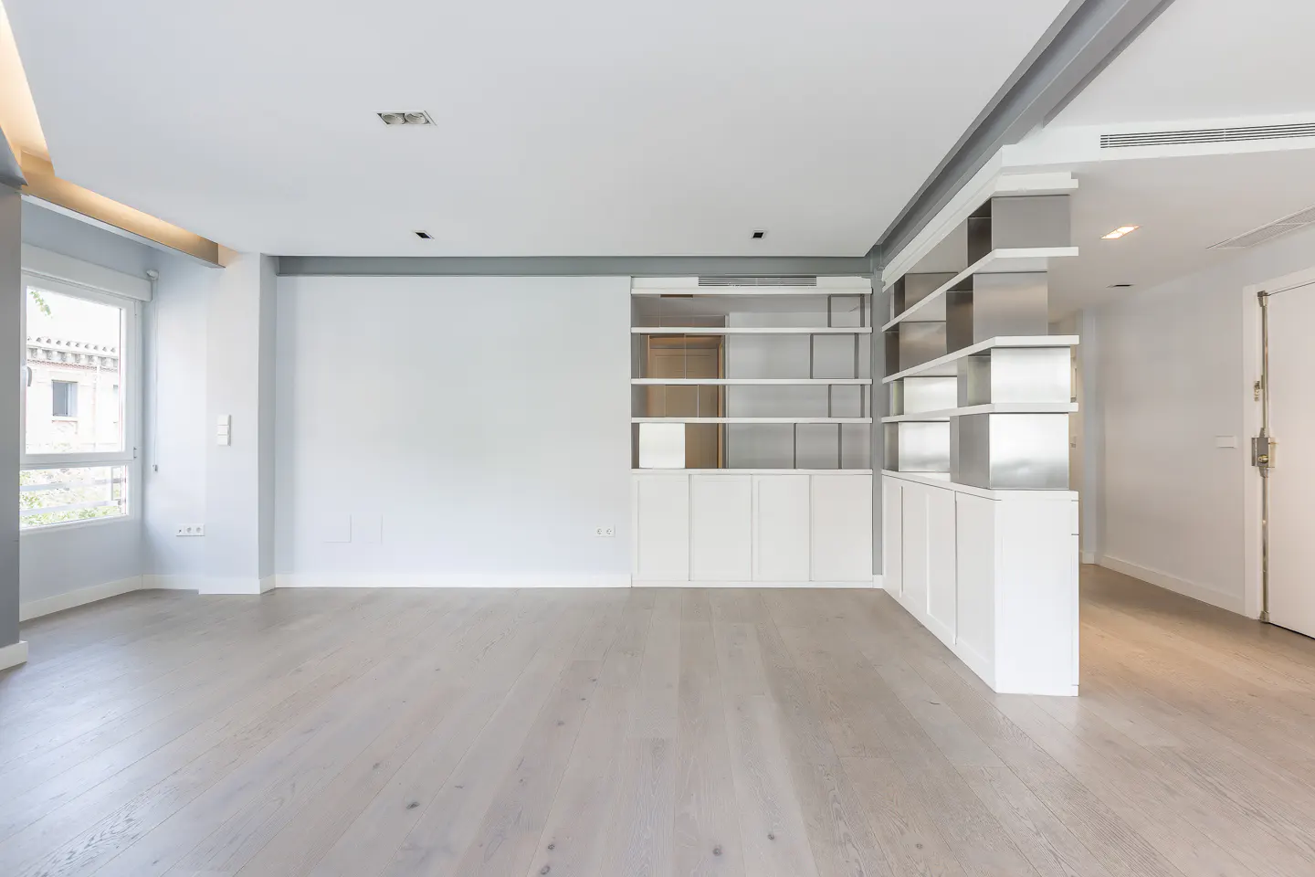 Bright, empty room with light wood floors, white walls, and a modern white and metallic shelving unit.