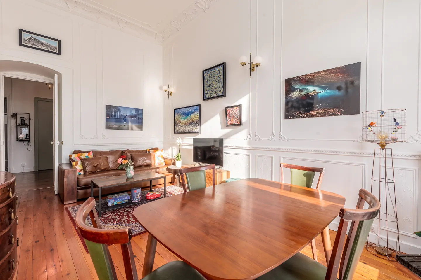 Bright living and dining room with white walls, wood floors, a brown leather sofa, and a wooden dining table with chairs.