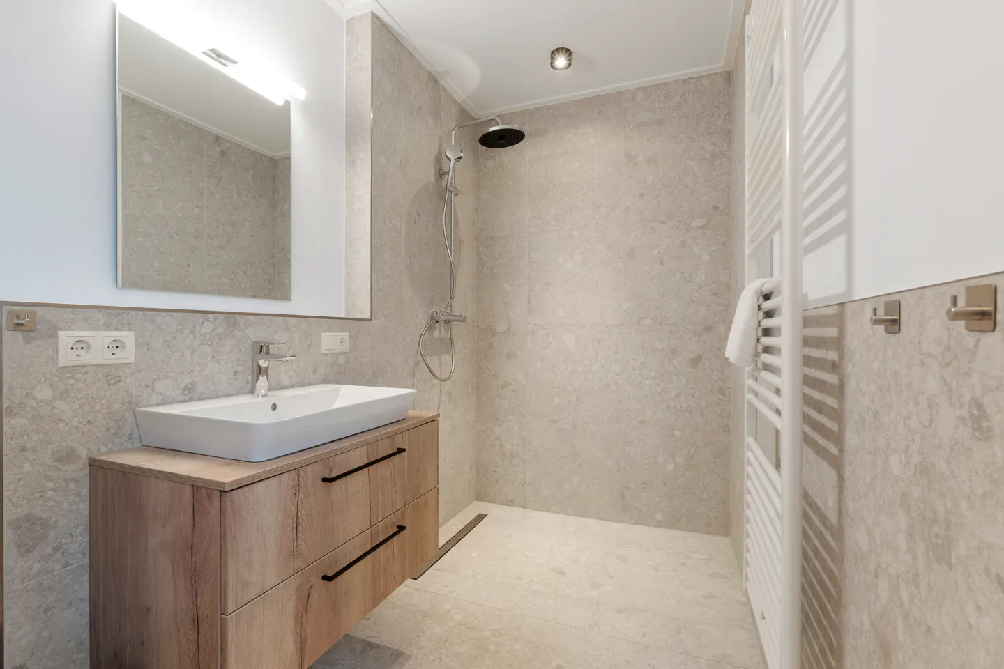 Modern bathroom with gray stone walls, a wood vanity with a white sink, and a shower with a rainfall showerhead.