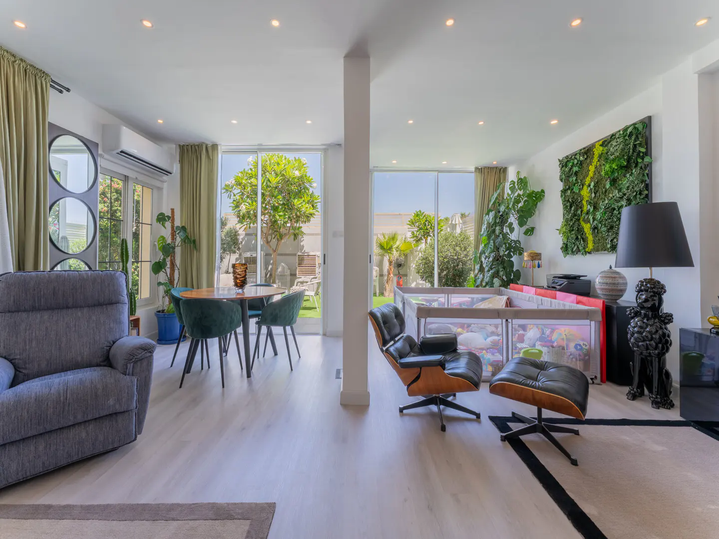 Bright, open living space with a gray recliner, round table with green chairs, and a black leather chair with ottoman. Large windows view the backyard.