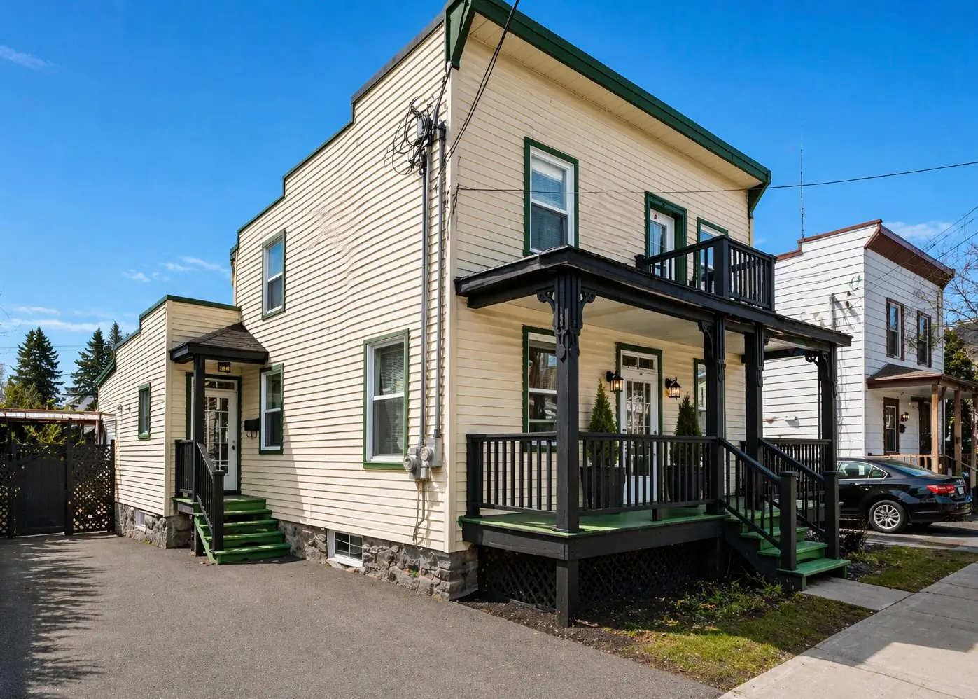 Two-story house with cream siding, green trim, and black porch. A black car is parked on the street.