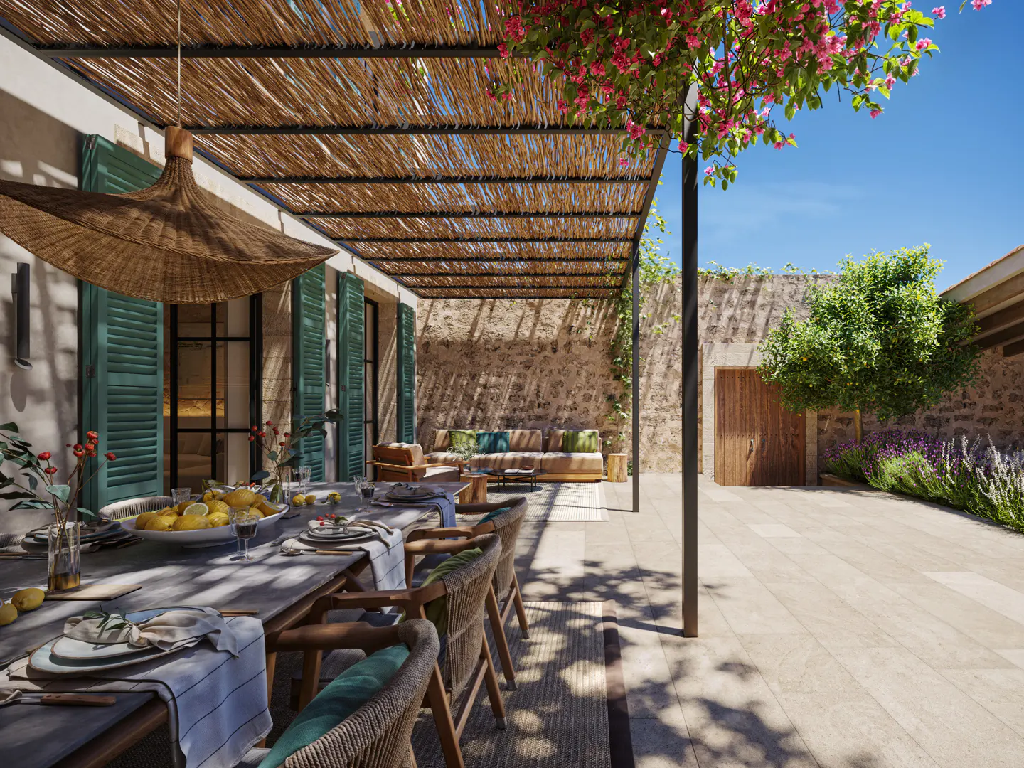Outdoor patio with a long dining table set for a meal, under a thatched pergola with pink flowers. Stone wall and garden in the background.