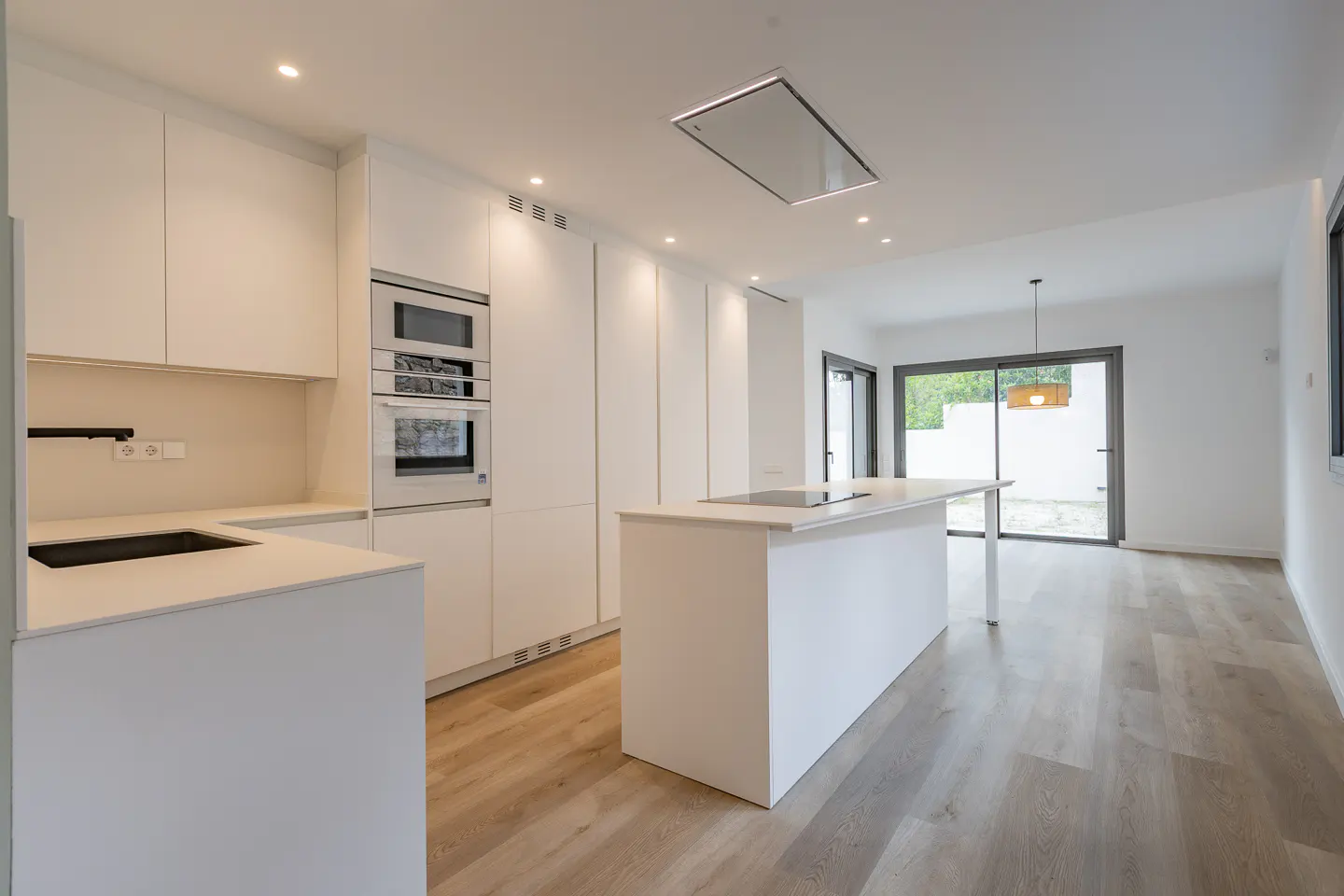 Bright, modern kitchen with white cabinets, island, and stainless steel appliances. Wood-look floors lead to sliding glass doors.
