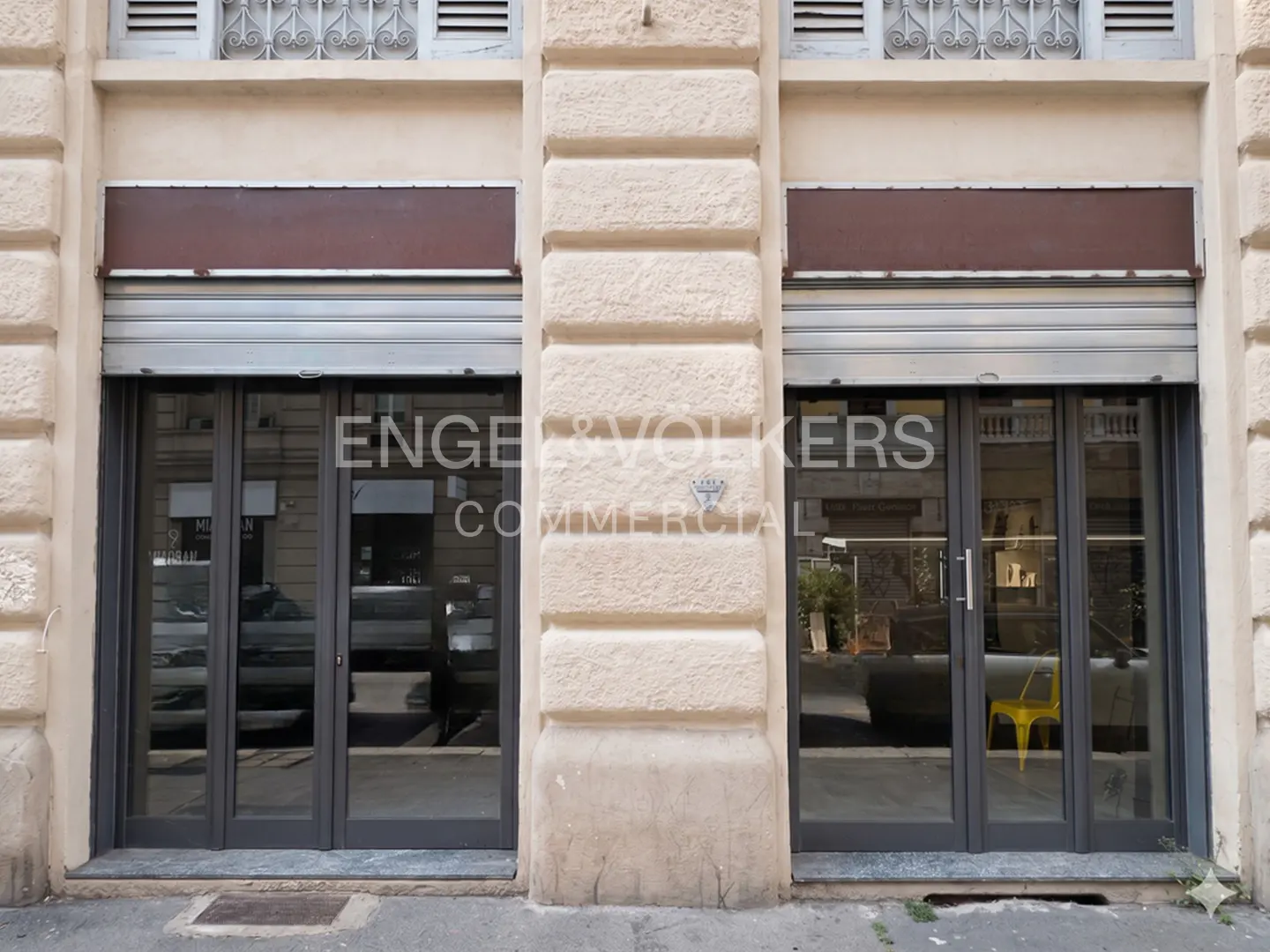 Commercial building facade with two storefronts, gray doors, and metal security shutters.