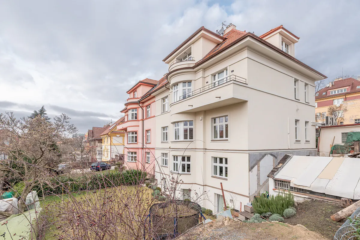 Exterior view of a multi-story cream-colored apartment building with curved balconies and a small backyard garden.