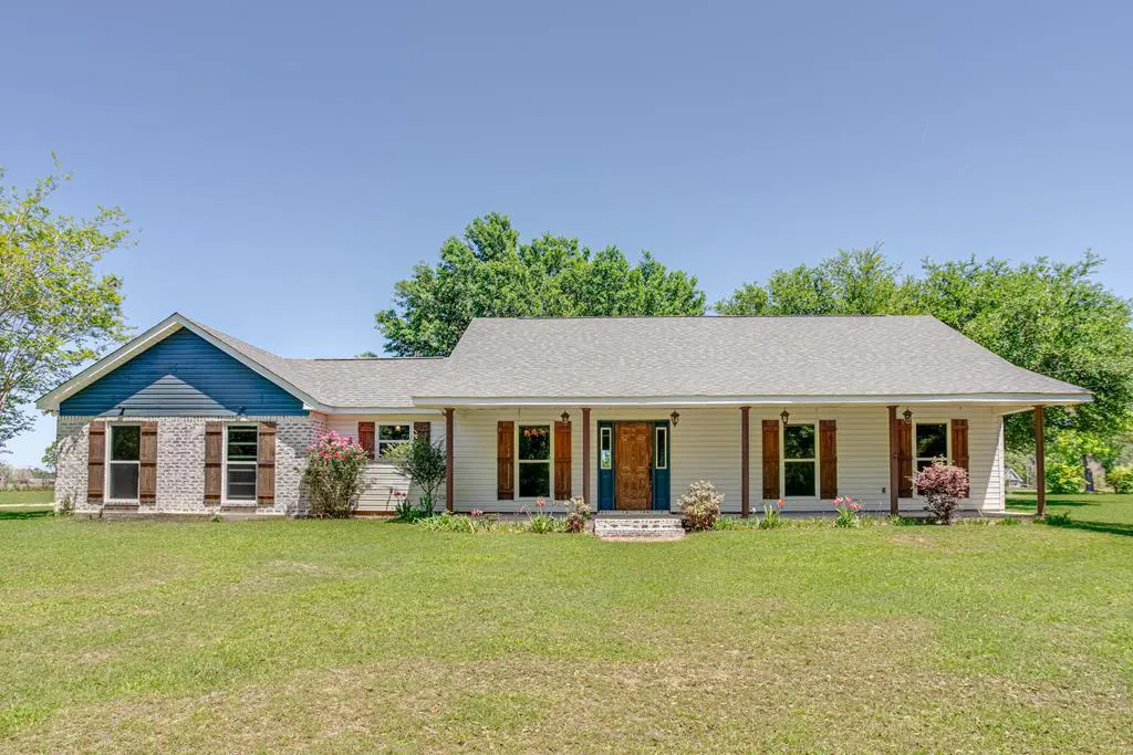 A single-story house with a blue door, brown shutters, and a large green lawn.