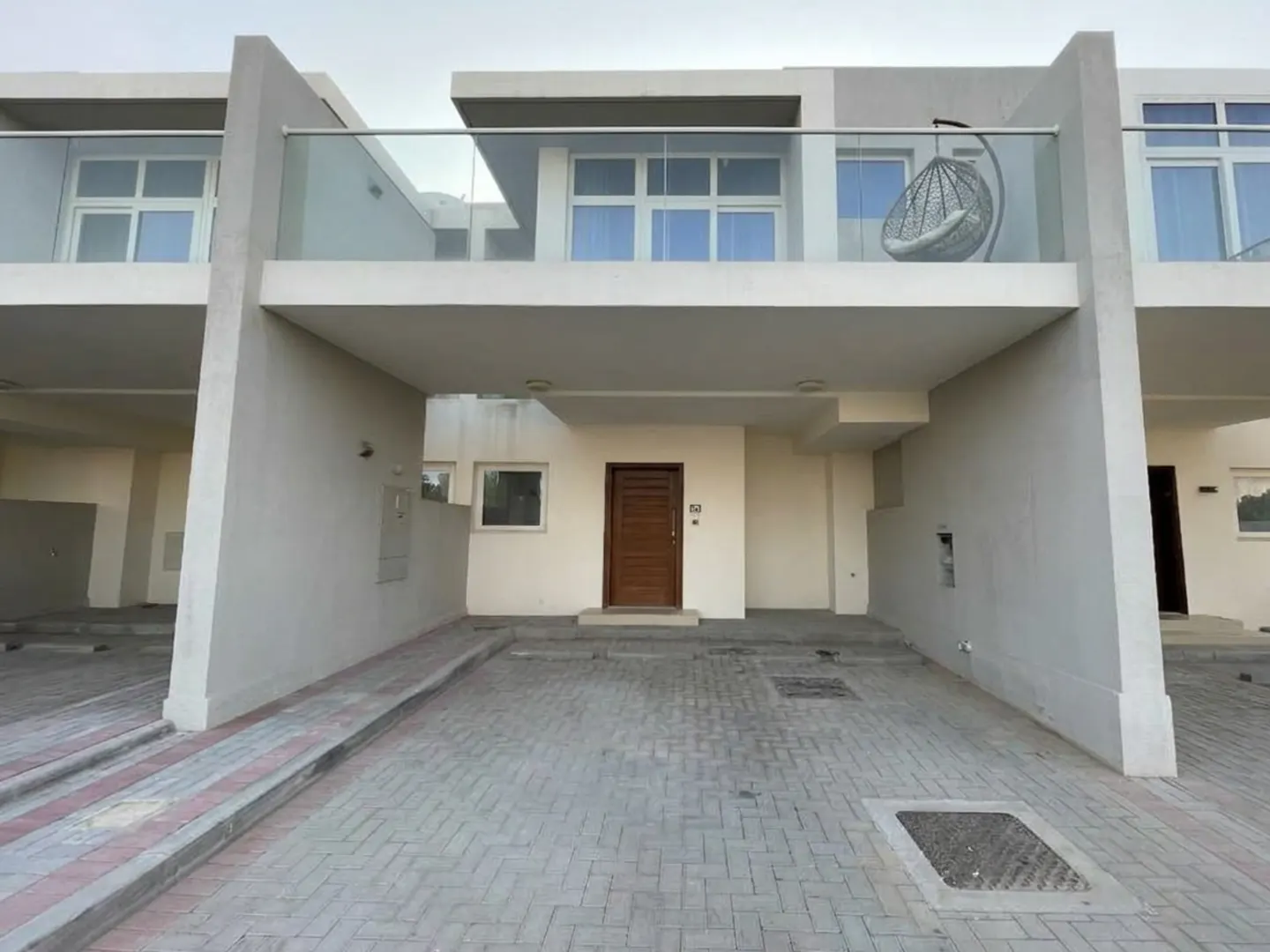 Exterior of a modern two-story townhouse with a brown front door and a balcony with a hanging chair.