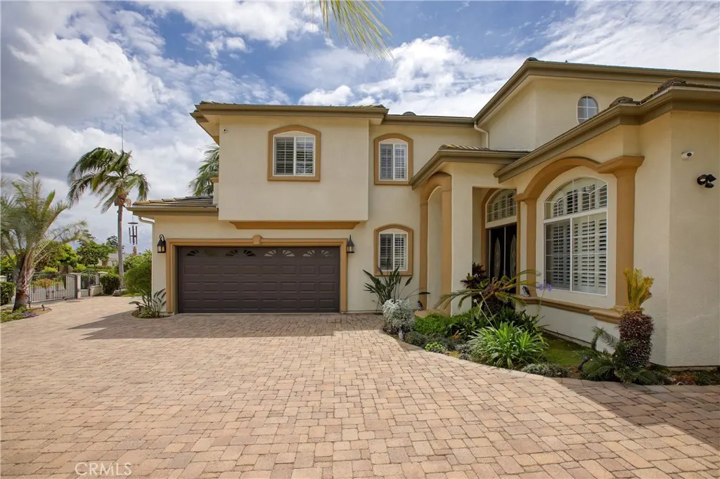 Two-story beige house with a brown garage door and brick driveway on a sunny day.