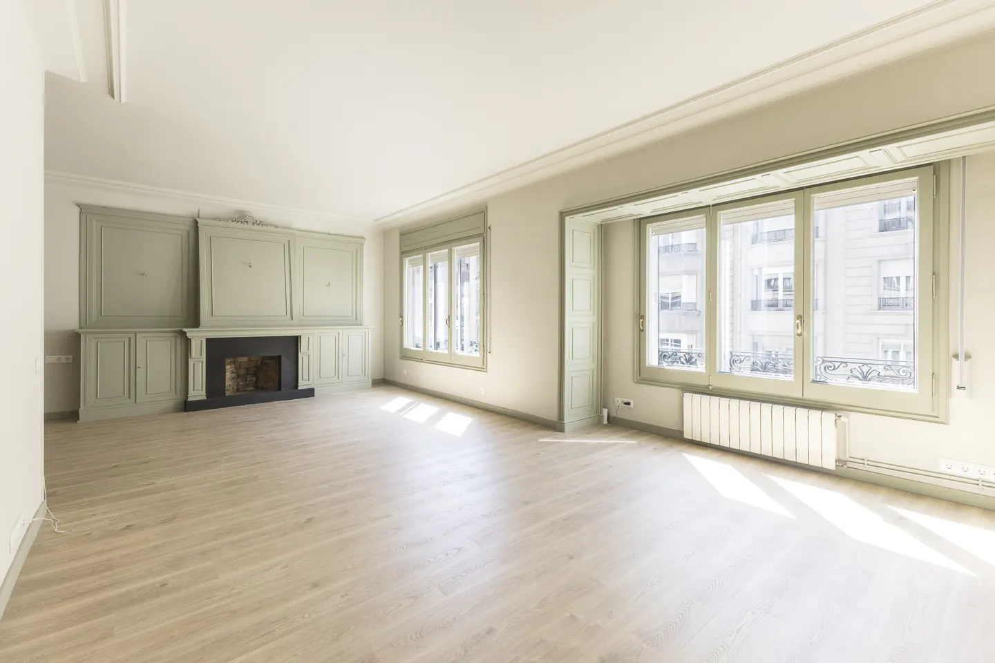 Bright, empty living room with light wood floors, large windows, and a decorative green fireplace with built-in cabinets.